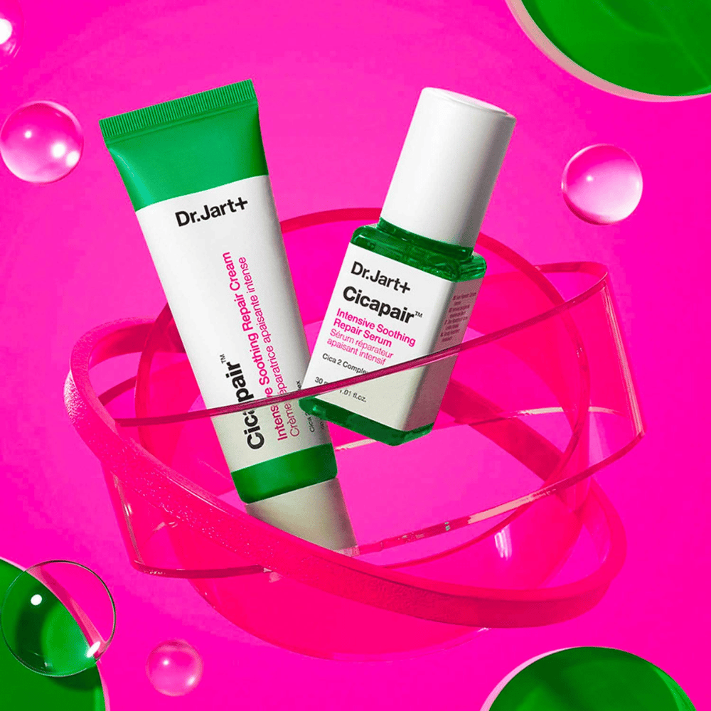 Dr.Jart+ Cicapair Intensive Soothing Repair Cream og Serum i grønne pakker, som står på en lyserød cirkulær base. Produkterne er udviklet til at berolige og reparere irriteret hud.
