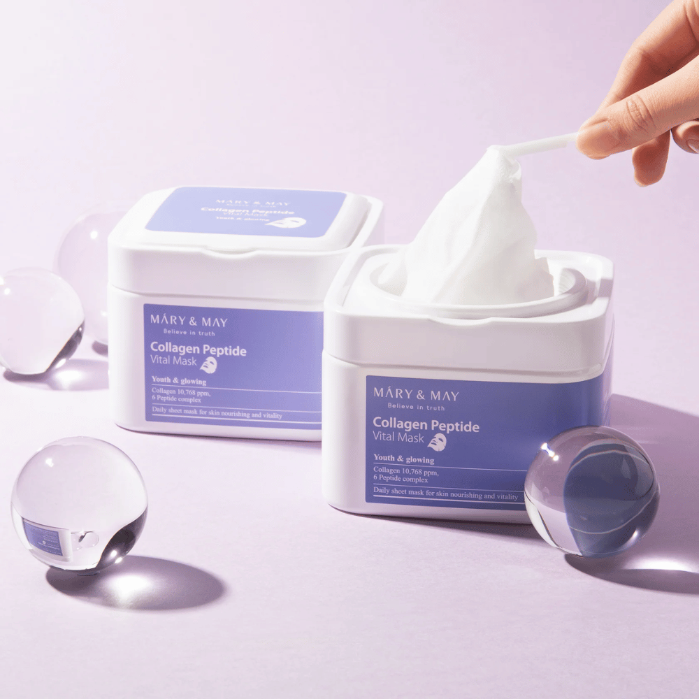 En hånd tager en maske op fra en krukke med MARY & MAY Collagen Peptide Vital Mask. Masken er beregnet til daglig brug for at give næring og glød til huden, med kollagen og peptider for at støtte hudens ungdommelighed.