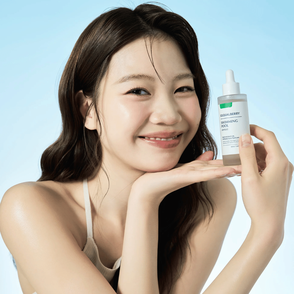 Smilende kvinde, der holder Eqqualberry Swimming Pool Ampoule, et fugtgivende hudplejeprodukt, med begge hænder foran en lyseblå baggrund.
