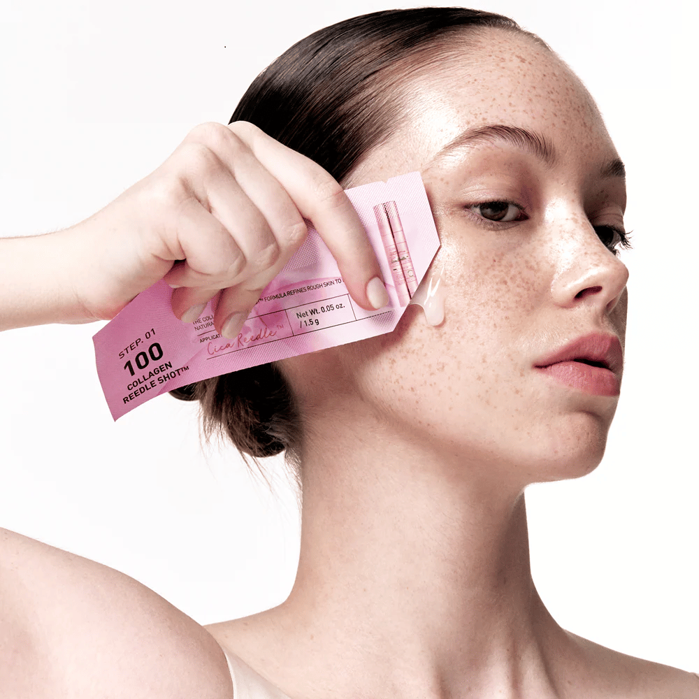 Kvinde anvender trin 1 af Collagen Reedle Shot 100 med en pink engangspakning på kinden. En klar gel ses på huden, hvilket markerer første trin i den to-trins hudplejebehandling.