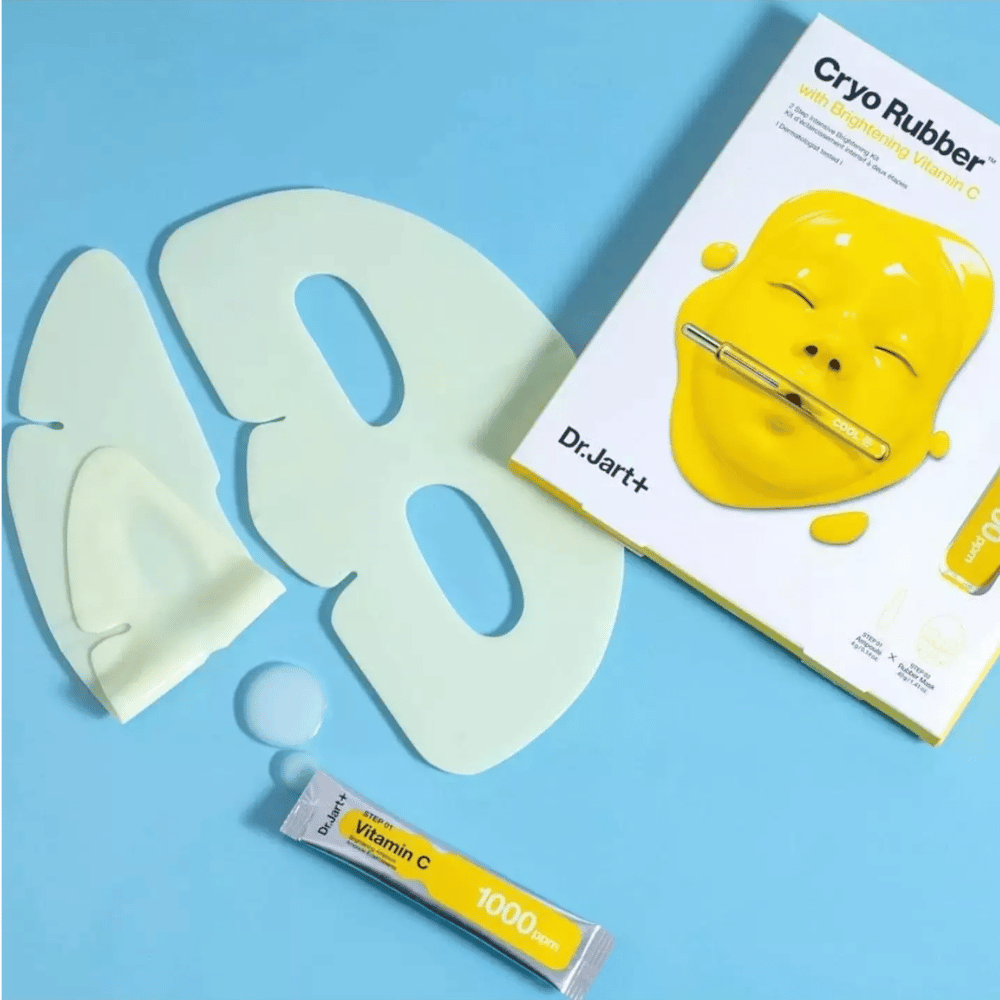 Billede af Dr.Jart+'s 'Cryo Rubber™ med Brightening Vitamin C' skønhedsprodukt. På en blå baggrund ses en hvid gummiansigtsmaske, en lille tube mærket 'Vitamin C 1000ppm', og en æske med produktets navn og billede af den gule maske.