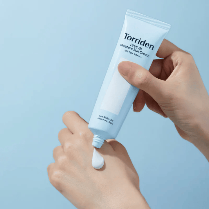 Torriden DIVE-IN Moisture Sun Cream SPF50+ PA++++ påføres på hånden for at vise den fugtgivende solcremes lette og cremede konsistens.