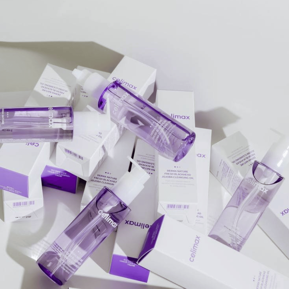 Celimax Derma Nature Fresh Blackhead Jojoba Cleansing Oil i lilla flasker placeret blandt hvide produkteemballager med lilla detaljer.