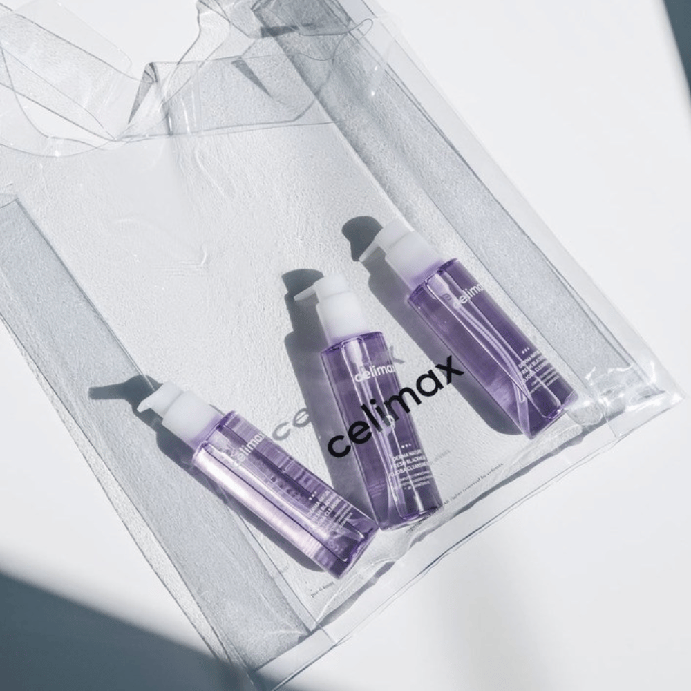 Tre flasker af Celimax Derma Nature Fresh Blackhead Jojoba Cleansing Oil i lilla emballage, placeret i en gennemsigtig pose med logoet 'celimax'.