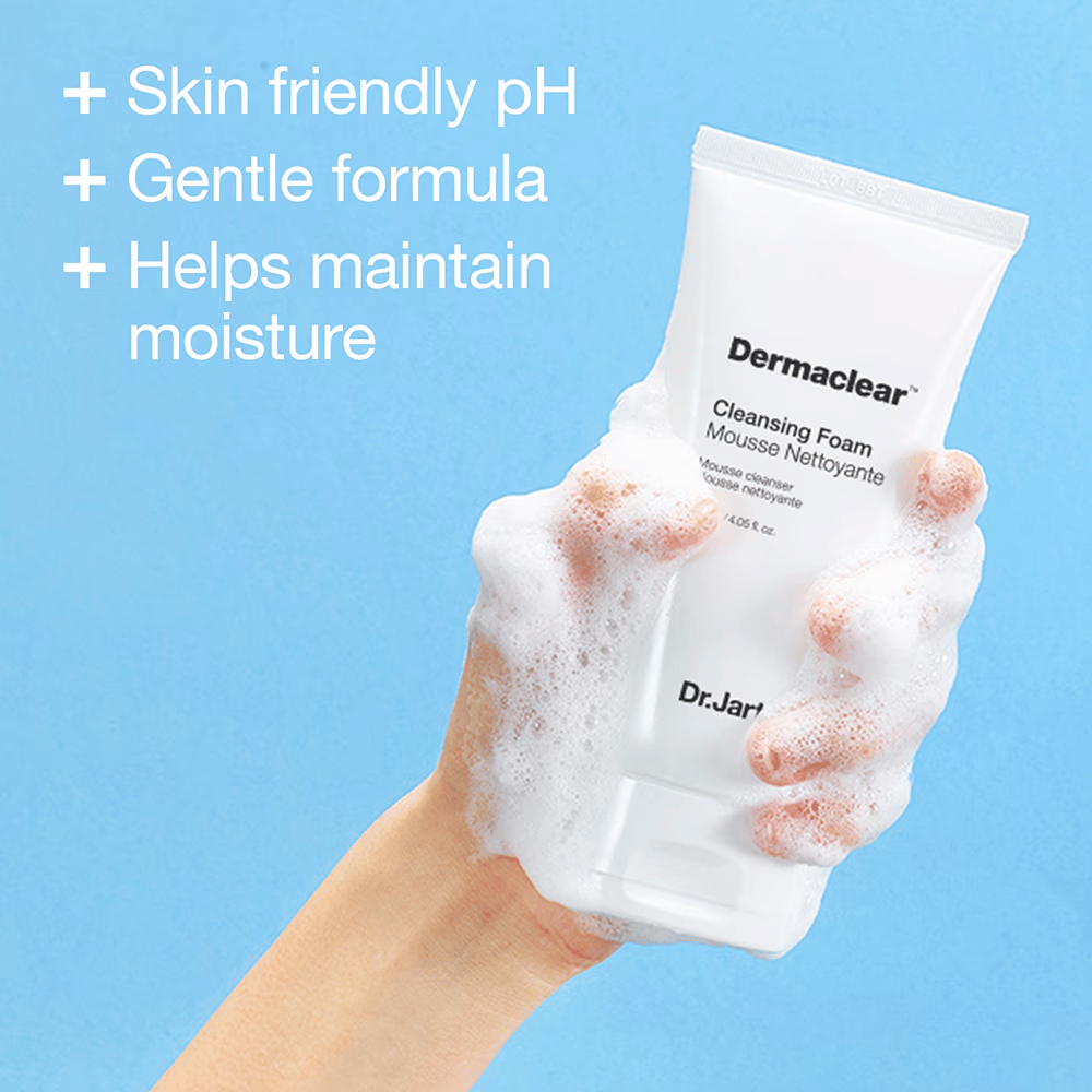 Hånd dækket af skum holder i Dr.Jart+ Dermaclear Cleansing Foam mod blå baggrund, med tekst der fremhæver hudvenligt pH, mild formel og fugtbevarende egenskaber.