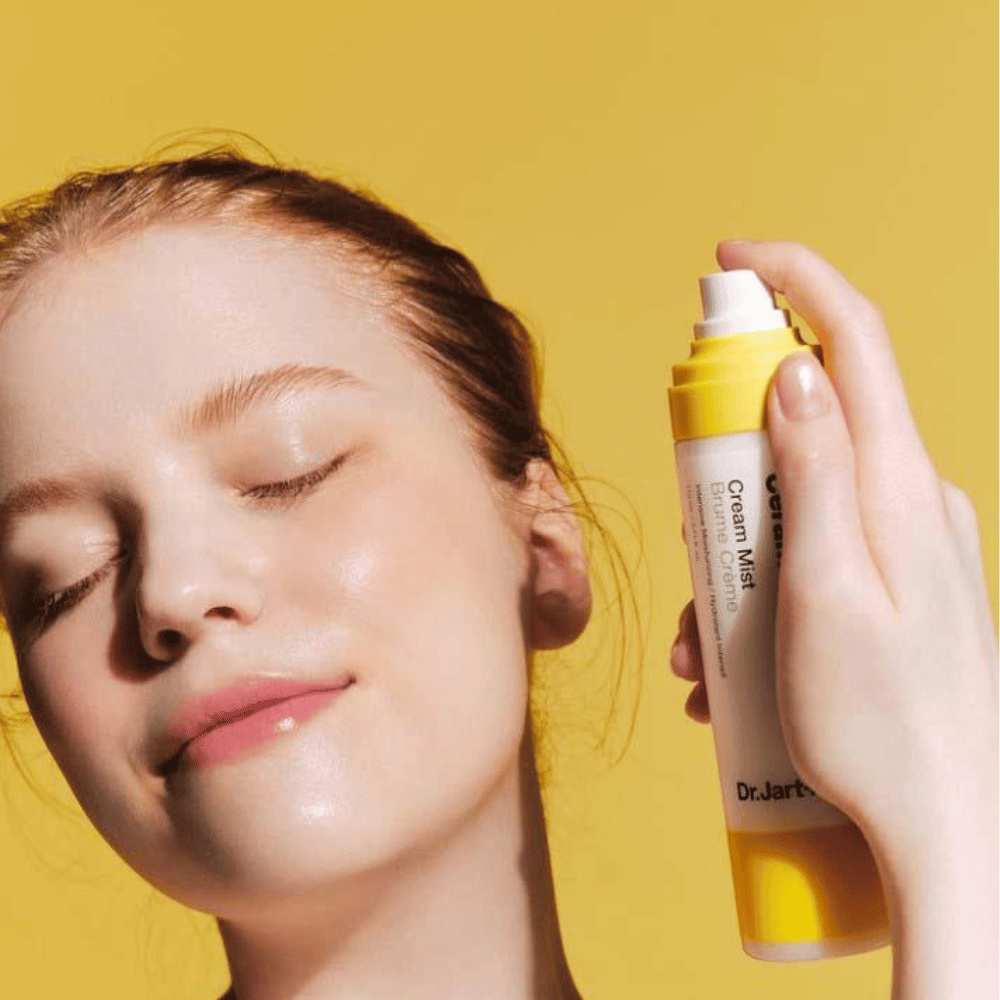 En kvinde holder en flaske Dr. Jart+ Ceramidin Cream Mist 110ml i ansigtet, hvilket fremmer dens fugt-boost-fordele og veganske formulering.