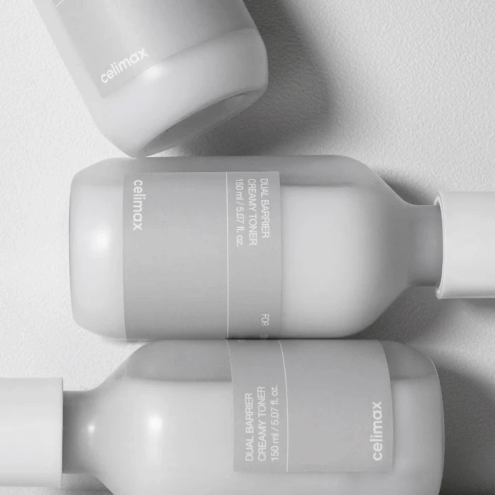 Tre liggende flasker af Celimax Dual Barrier Creamy Toner i et minimalistisk design med grå etiket og blødt lys – perfekt til sensitiv og tør hud.