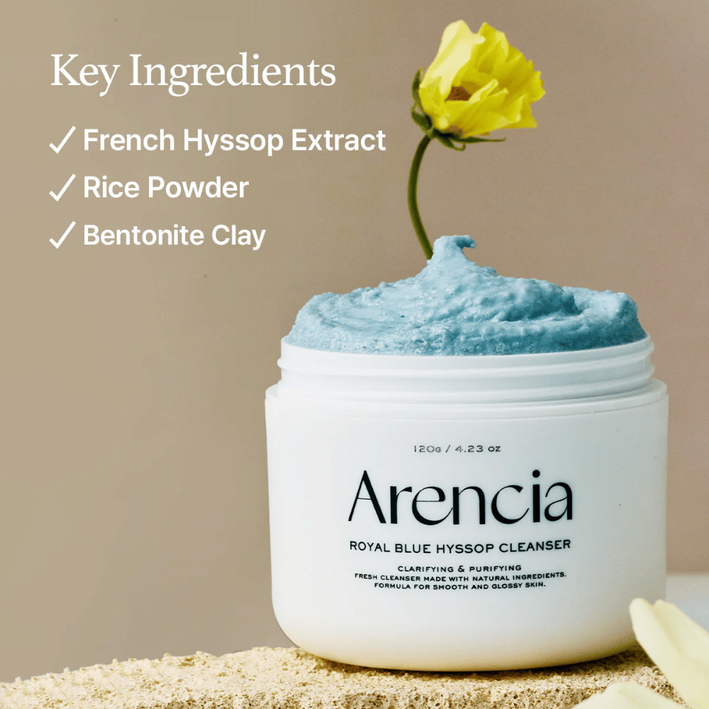 Billede af krukken "Arencia Royal Blue Hyssop Cleanser" fyldt med blå rengøringscreme. En gul blomst stikker op af cremen. Teksten i billedet fremhæver tre nøgleingredienser: French Hyssop Extract, Rice Powder og Bentonite Clay.