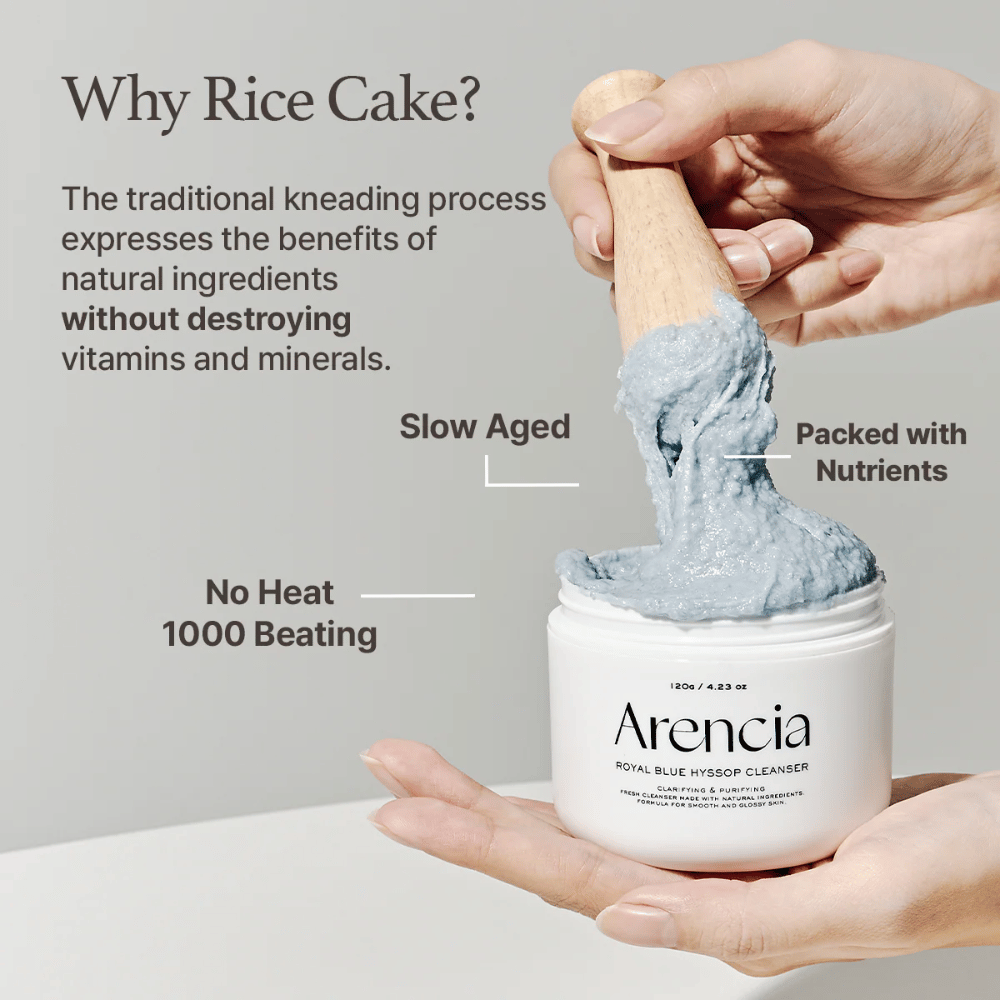 Hånd der holder rengøringskrukken "Arencia Royal Blue Hyssop Cleanser" med en træske, der løfter den blå, mochi-lignende rengøringspasta. Tekst i billedet beskriver fordele ved risdejprocessen, såsom "No Heat", "1000 Beating", "Slow Aged" og "Packed with Nutrients".