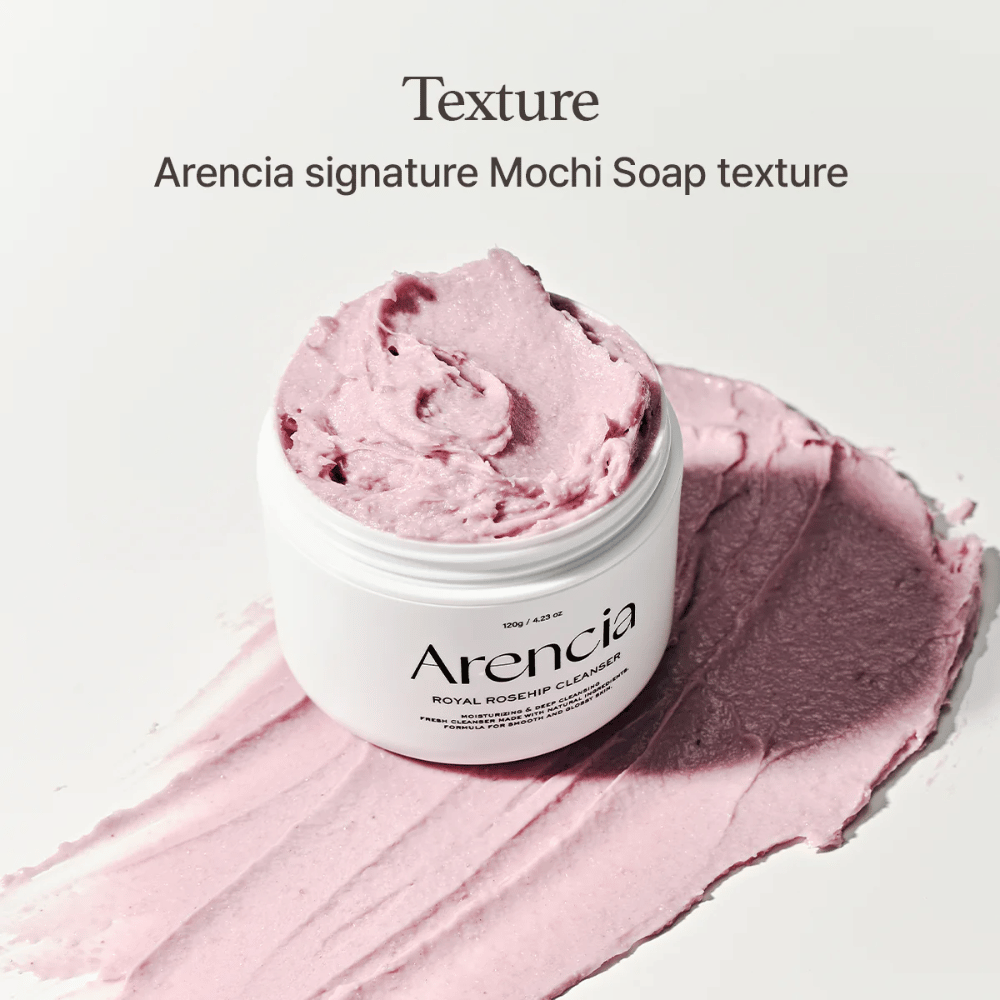 Krukke med Arencia Royal Rosehip Cleanser ses ovenpå en udsmurt lyserød rens med mochi-lignende tekstur. Teksten ovenfor beskriver produktet som Arencias signaturtekstur.