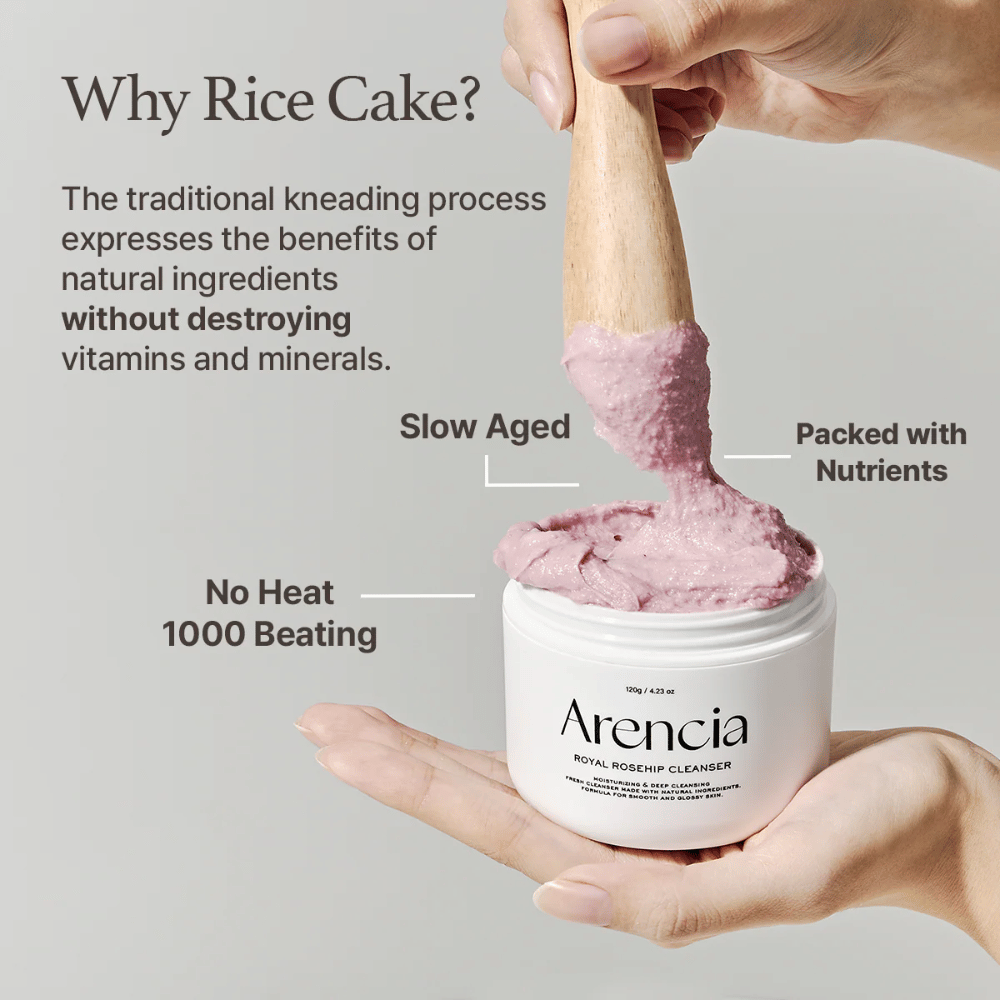 En hånd holder en åben krukke af Arencia Royal Rosehip Cleanser, med en lyserød, mochi-lignende renseformel, der løftes med en træspatel – viser produktets tekstur og traditionelle fremstillingsmetode.