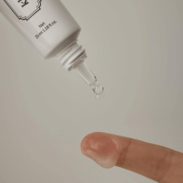 Detaljebillede, hvor en klar, let gel påføres fra den smalle spids mod en finger. Billedet illustrerer produktets transparente, gelbaserede konsistens og den præcise påføring omkring øjenområdet.