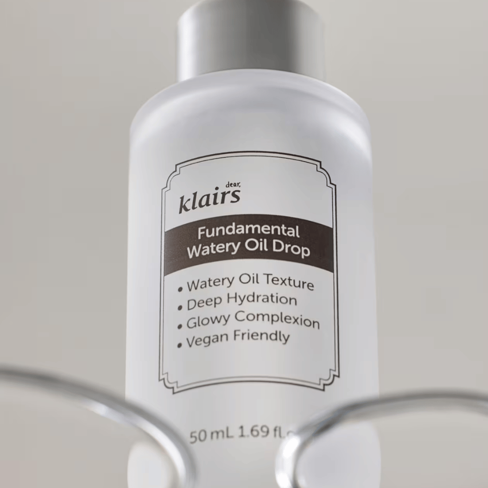 Flaske med Klairs Fundamental Watery Oil Drop, 50 ml, placeret i en gennemsigtig holder, med tydelig etiket der fremhæver produktets fugtgivende og veganske egenskaber.