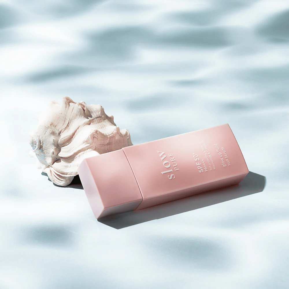 Slow Pure Glow Up Fluid Sun Serum ved muslingeskal og vandeffekt, fremhæver solbeskyttelse og glød.