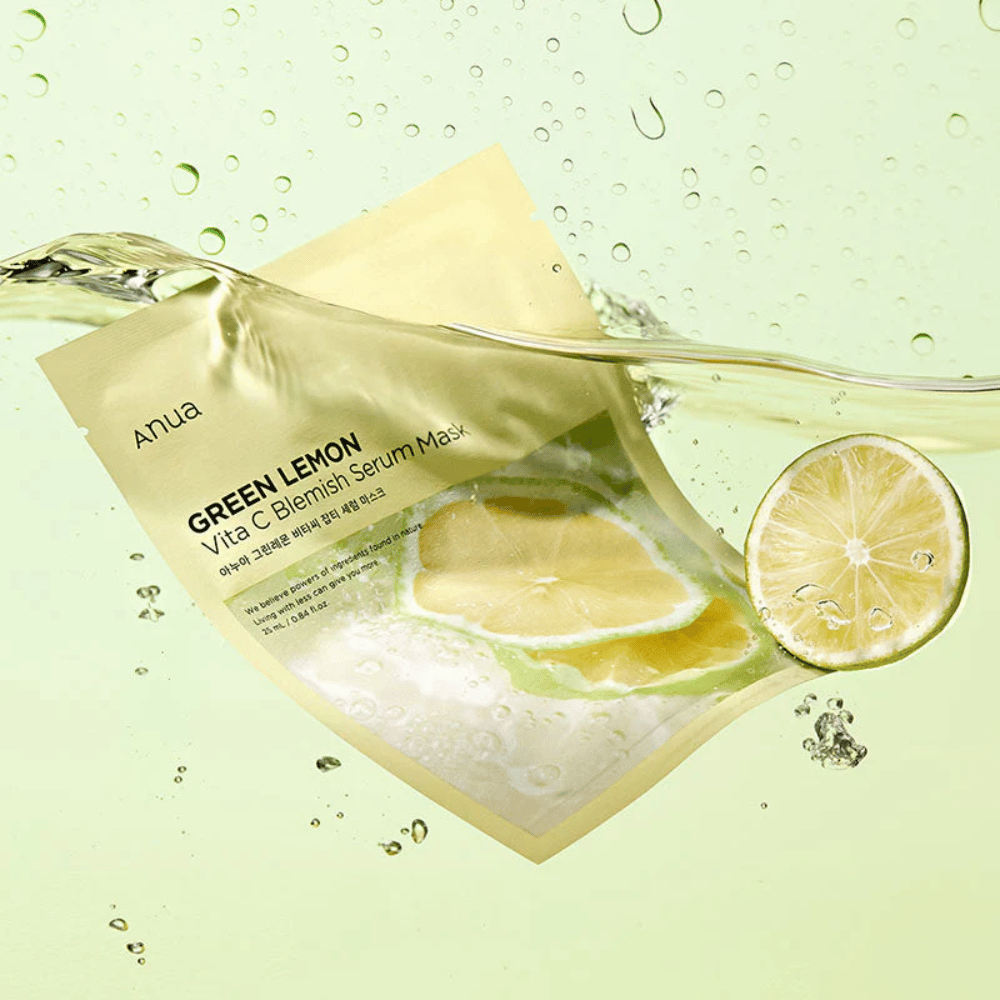 Et levende billede af Anua Green Lemon Vita C Blemish Serum Mask emballage med gennemsigtige vanddråber og skiver af grøn citron rundt omkring. Emballagen er delvist dækket af en strøm af vand på en lysegrøn baggrund.