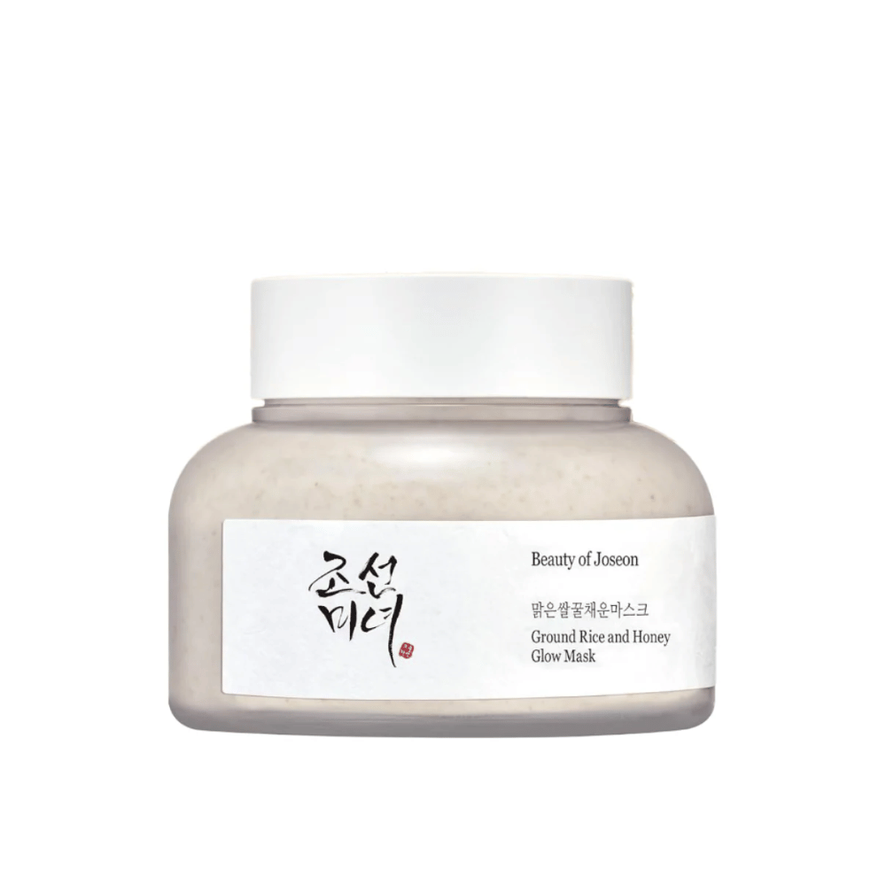 En krukke "Beauty of Joseon Ground Rice and Honey Glow Mask". Emballagen er enkel med en hvid kork og en etiket, der præsenterer produktnavnet og ingredienser på både koreansk og engelsk. Produktet er designet til at give glans og næring til huden.