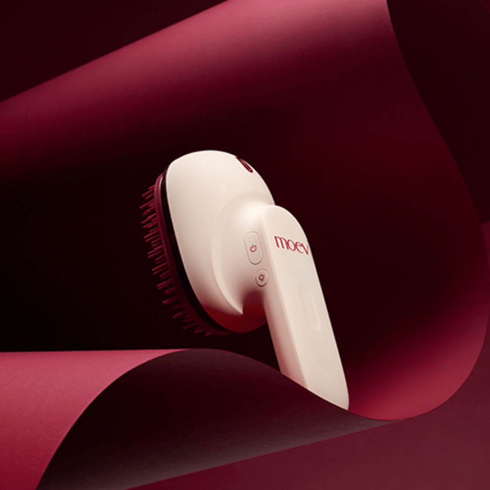 MOEV Hair Steamer Pro i elegant design mod rød baggrund. Innovativ hårplejebørste, der bruger damp og varme til at give glans, blødhed og styrket hårsundhed.