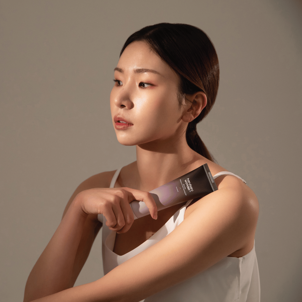 En ung asiatisk kvinde, der holder en børste i hånden, mens hun bruger Haruharu Wonders Black Rice Moisture 5.5 Soft Cleansing Gel 100ml.