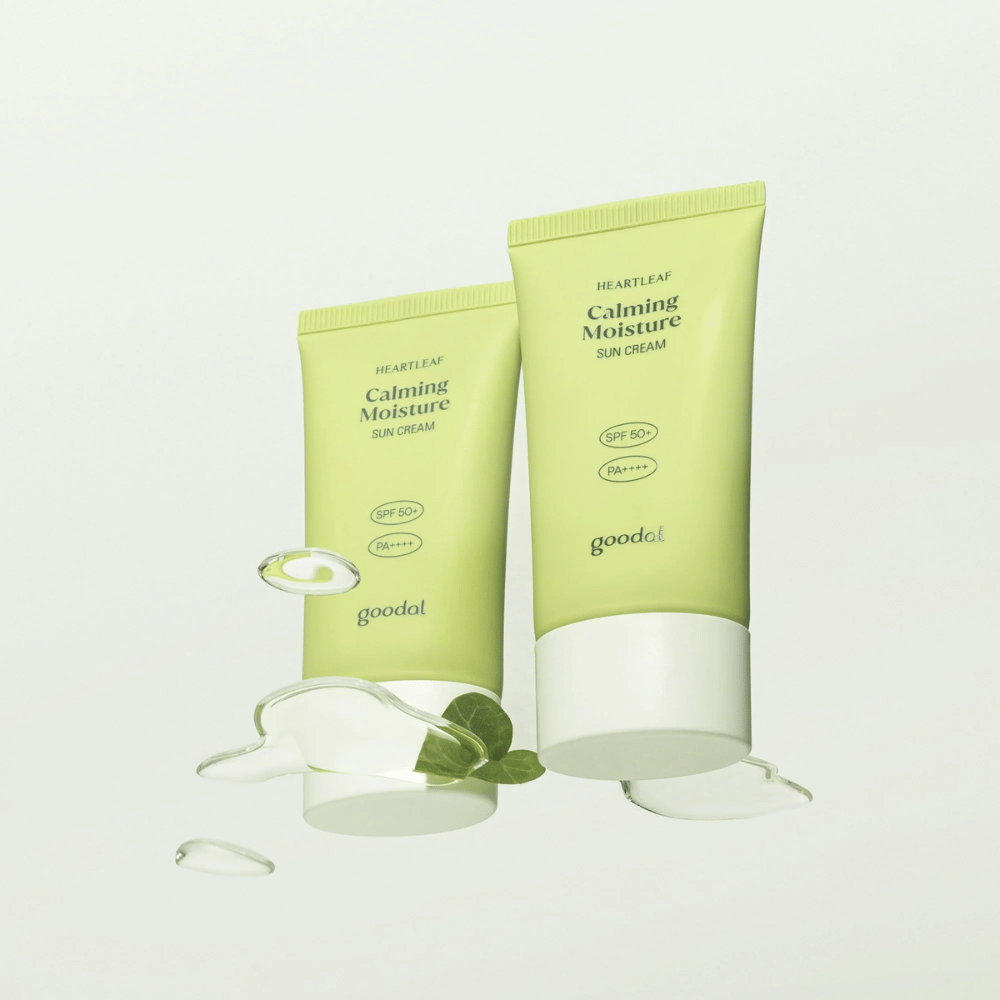 To tuber af Goodal Heartleaf Calming Moisture Sun Cream SPF50+ PA++++ omgivet af planteblade og serumdråber mod lys baggrund.