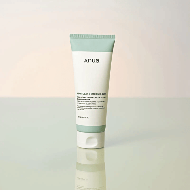 Fritstående produktbillede af Anua Heartleaf + Succinic Acid Moisture Cleansing Foam. Produktet vises stående på en reflekterende overflade, som tydeligt fremhæver emballagens design og brandets stilrene æstetik.