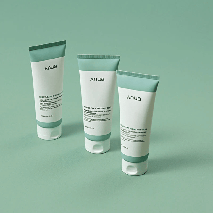 Tre pakninger af Anua Heartleaf + Succinic Acid Moisture Cleansing Foam præsenteret mod en lysegrøn baggrund. Billedet fremhæver produktets rene og minimalistiske design samt giver et professionelt indtryk af produktserien.