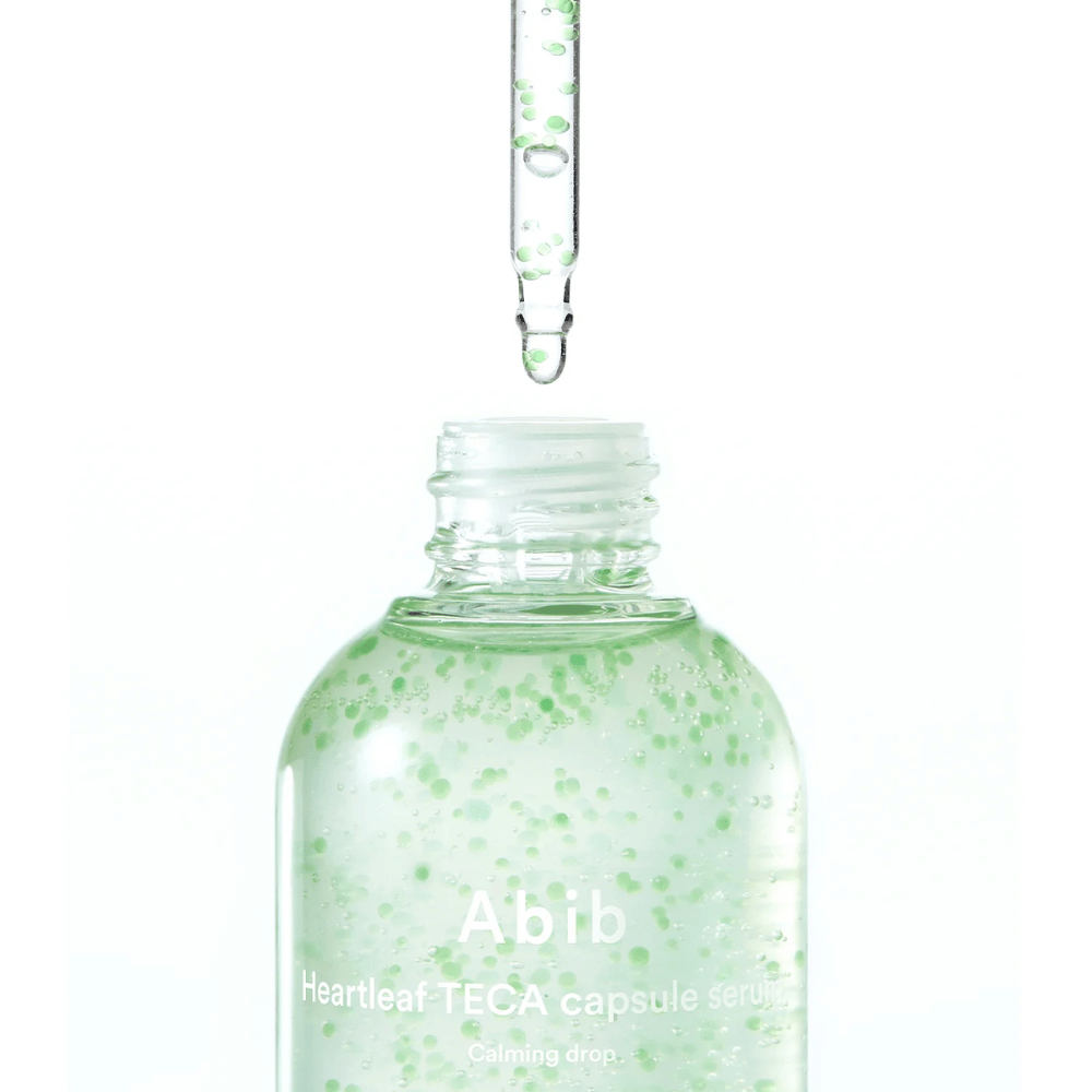 Minimalistisk nærbillede af serumflaske og pipette, hvor den transparente formel med grønne kapsler er i fokus mod en lys baggrund.