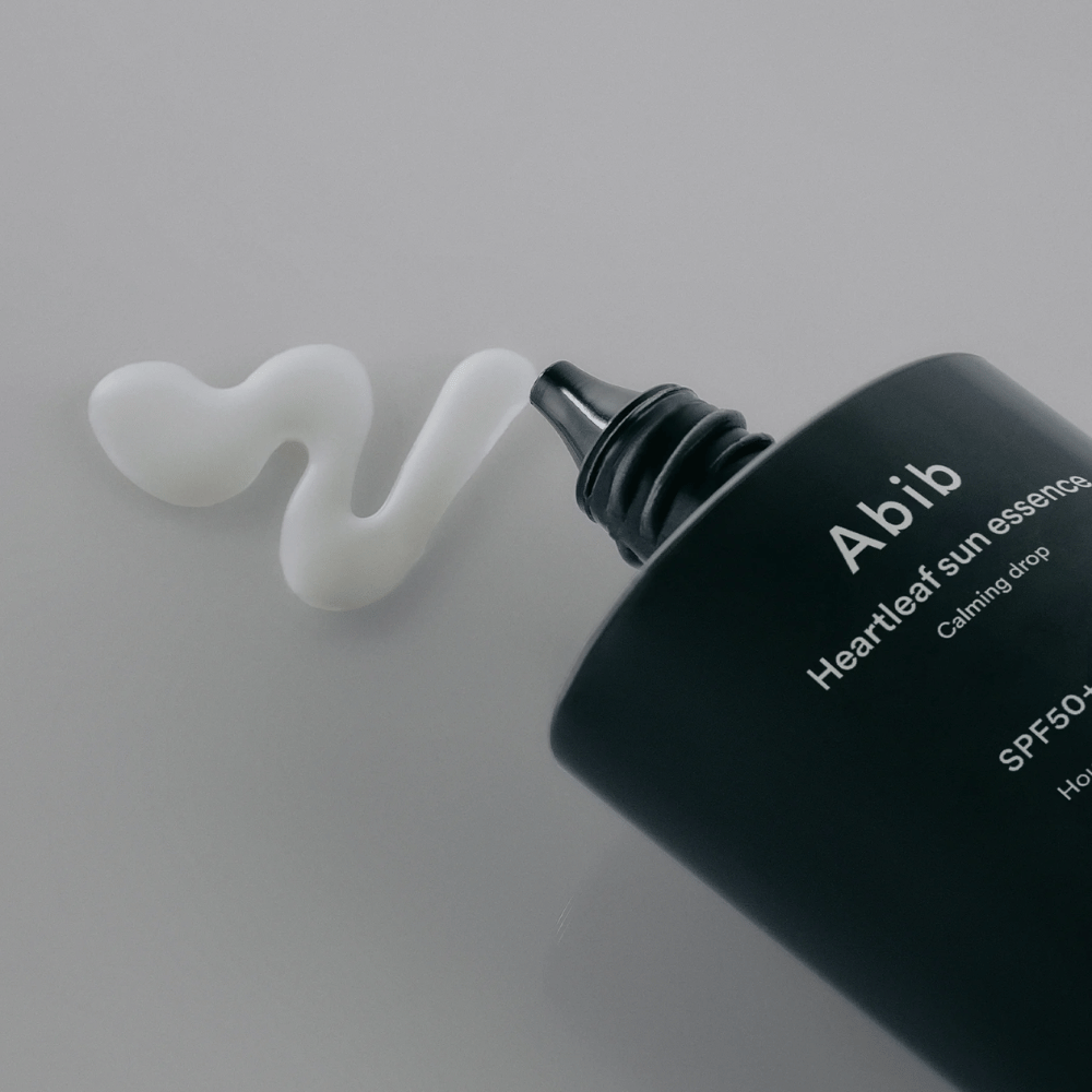 Nærbillede af Abib Heartleaf Sun Essence Calming Drop med solcremen presset ud i en hvid, bølget linje på en lys overflade.