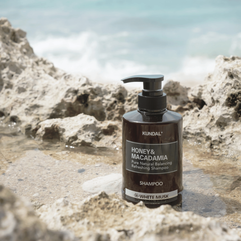 KUNDAL Honey & Macadamia Nature Shampoo White Musk placeret på klipper ved havet, et naturligt hårplejeprodukt med frisk duft.
