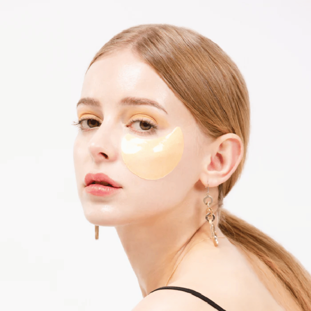 Model bærer et guldfarvet hydrogel eye patch under øjet for en lysende effekt.