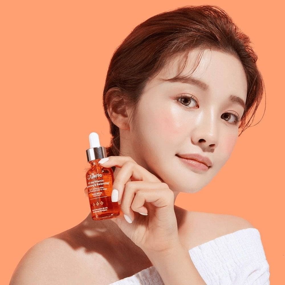 En kvinde, der holder en flaske JUMISO All Day Vitamin Brightening & Balancing Facial Serum 30ml.