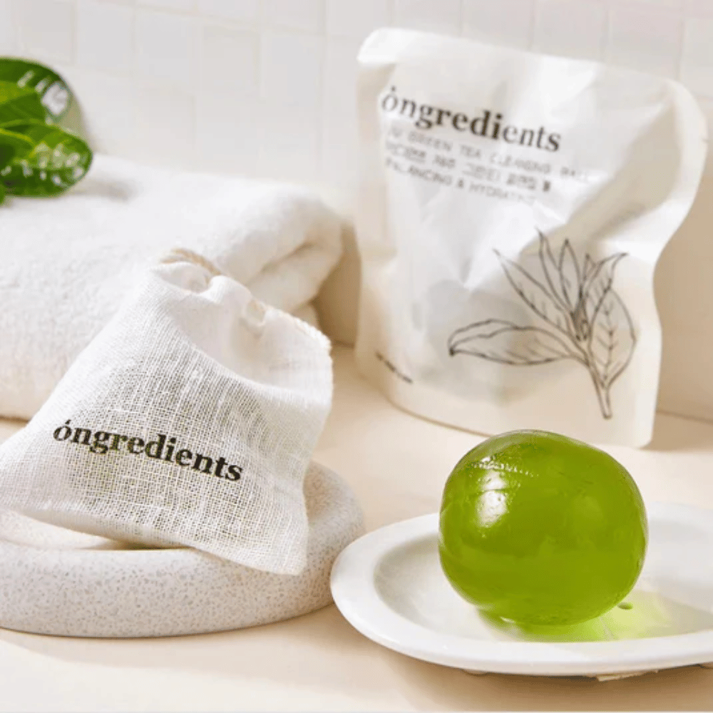 Óngredients Jeju Green Tea Cleansing Ball placeret på fad med emballage og håndklæde – skånsom rens med grøn te fra Jeju.