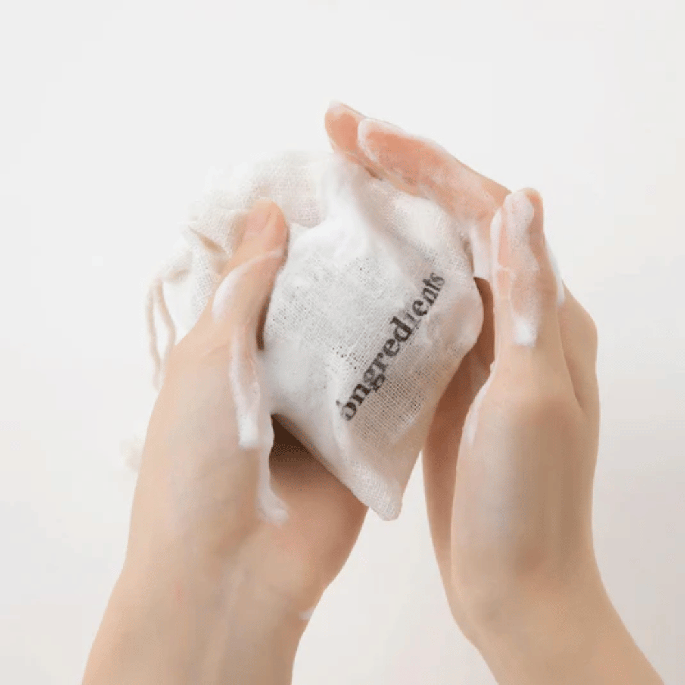 Hænder, der skummer Óngredients Jeju Green Tea Cleansing Ball i stofpose – vegansk ansigtsrens med grøn te.