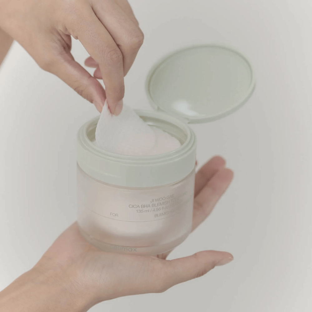 Hånd tager en toner pad op fra dåsen Celimax Ji Woo Gae Cica BHA Blemish Toner Pad, perfekt til uren hud.