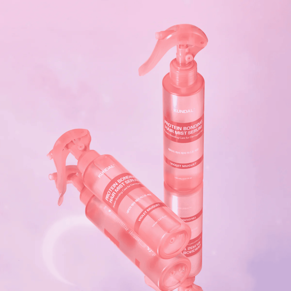 KUNDAL Protein Bonding Hair Mist Serum Violet Muguet i lyserøde sprayflasker, stående og liggende mod en lyserød baggrund med refleksion.