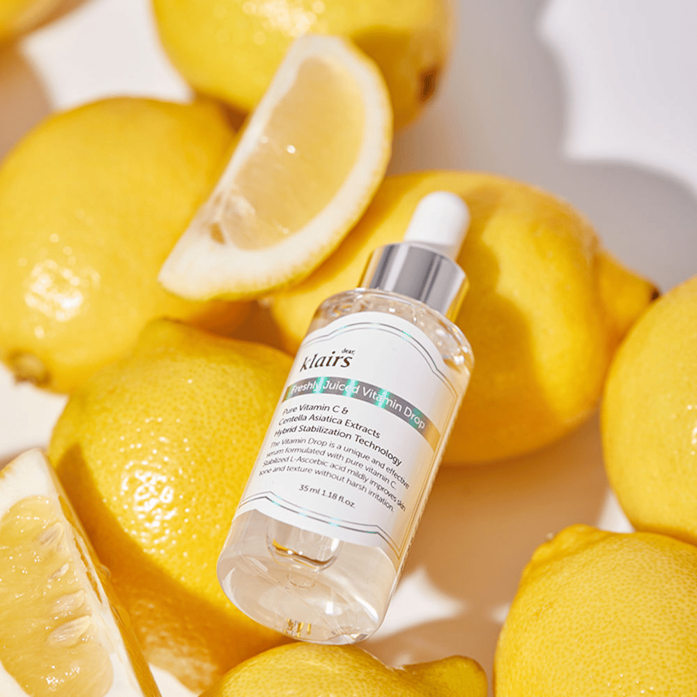 Klairs Freshly Juiced Vitamin Drop serumflaske omgivet af friske citronhalvdele og citronskiver på en lys overflade, fremhæver ingredienserne.