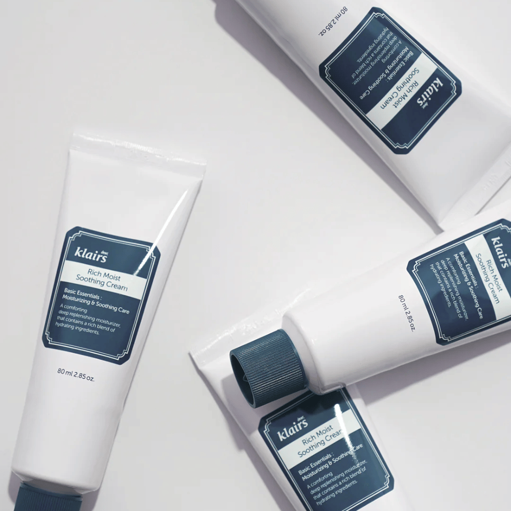 Flere rør af Klairs Rich Moist Soothing Cream strategisk placeret på en lys overflade, med skygger der skaber dybde.