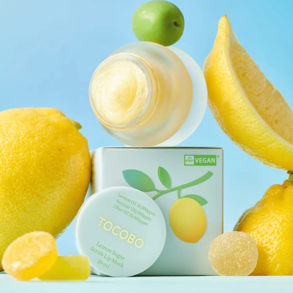 Krukke med Tocobo Lemon Sugar Scrub Lip Mask placeret blandt citroner og emballage, markeret som vegansk venlig.