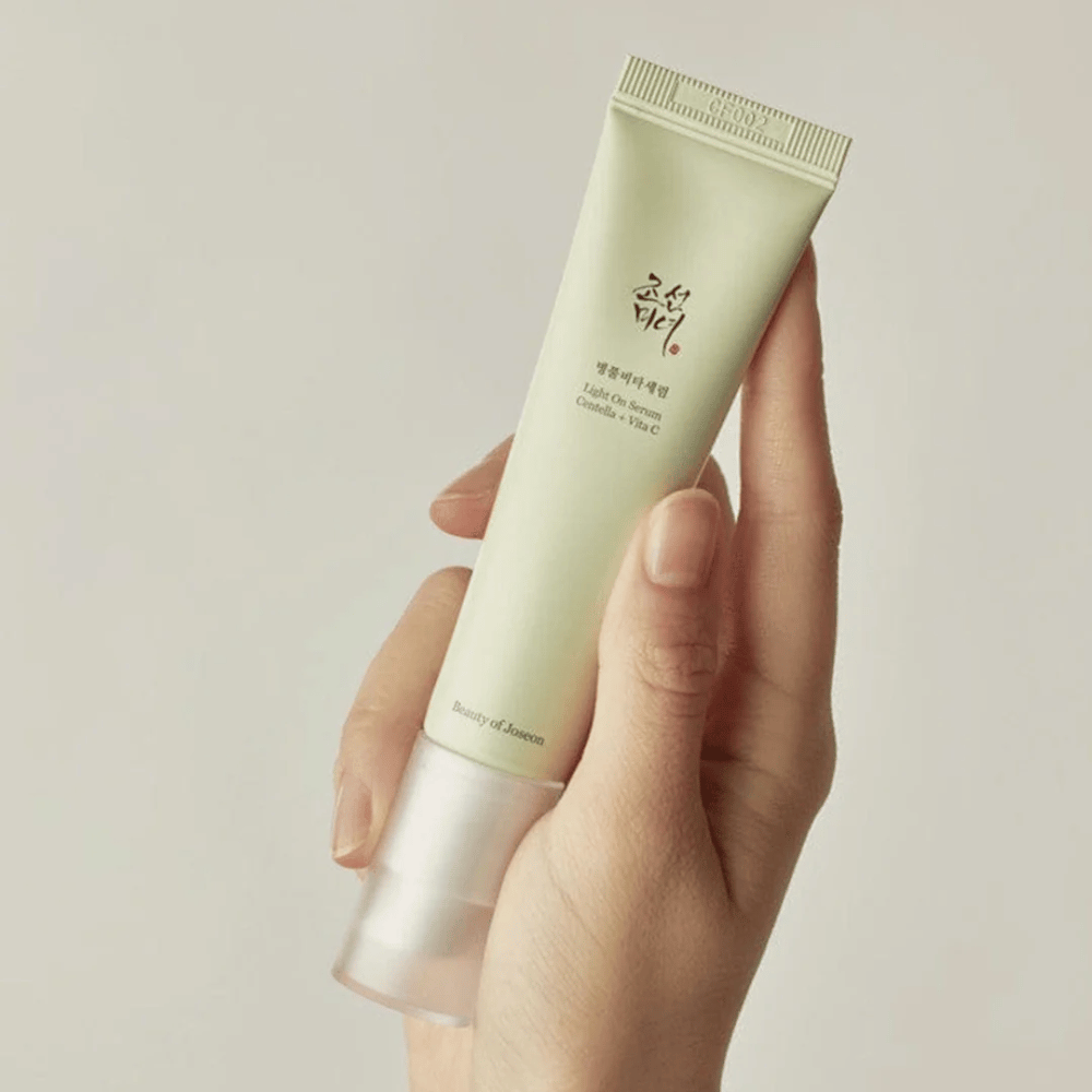 En hånd holder i Beauty of Joseon Light On Serum med Centella og vitamin C, i en lysegrøn tube med minimalistisk design mod en neutral baggrund.