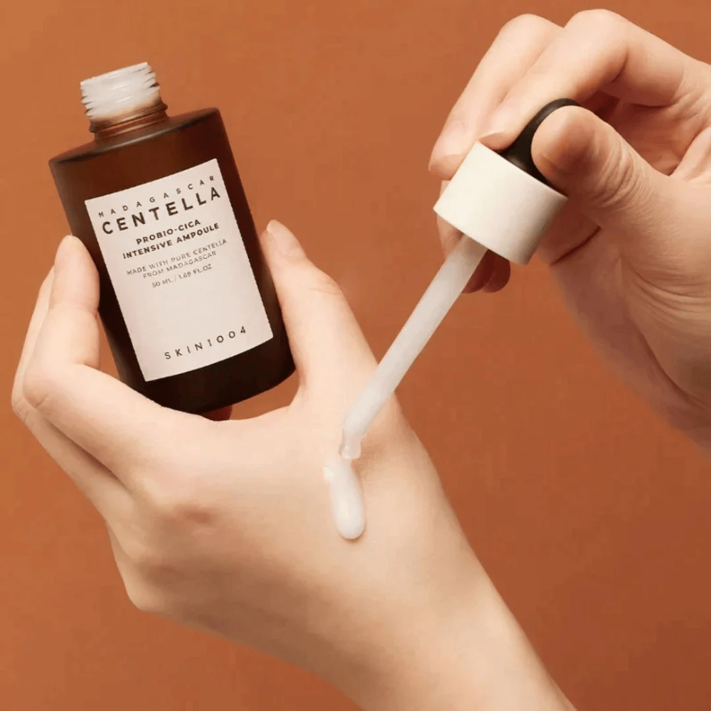 Hænder der bruger dråbepipette til at dosere "Madagascar Centella Probio-Cica Intensive Ampoule" fra SKIN1004.