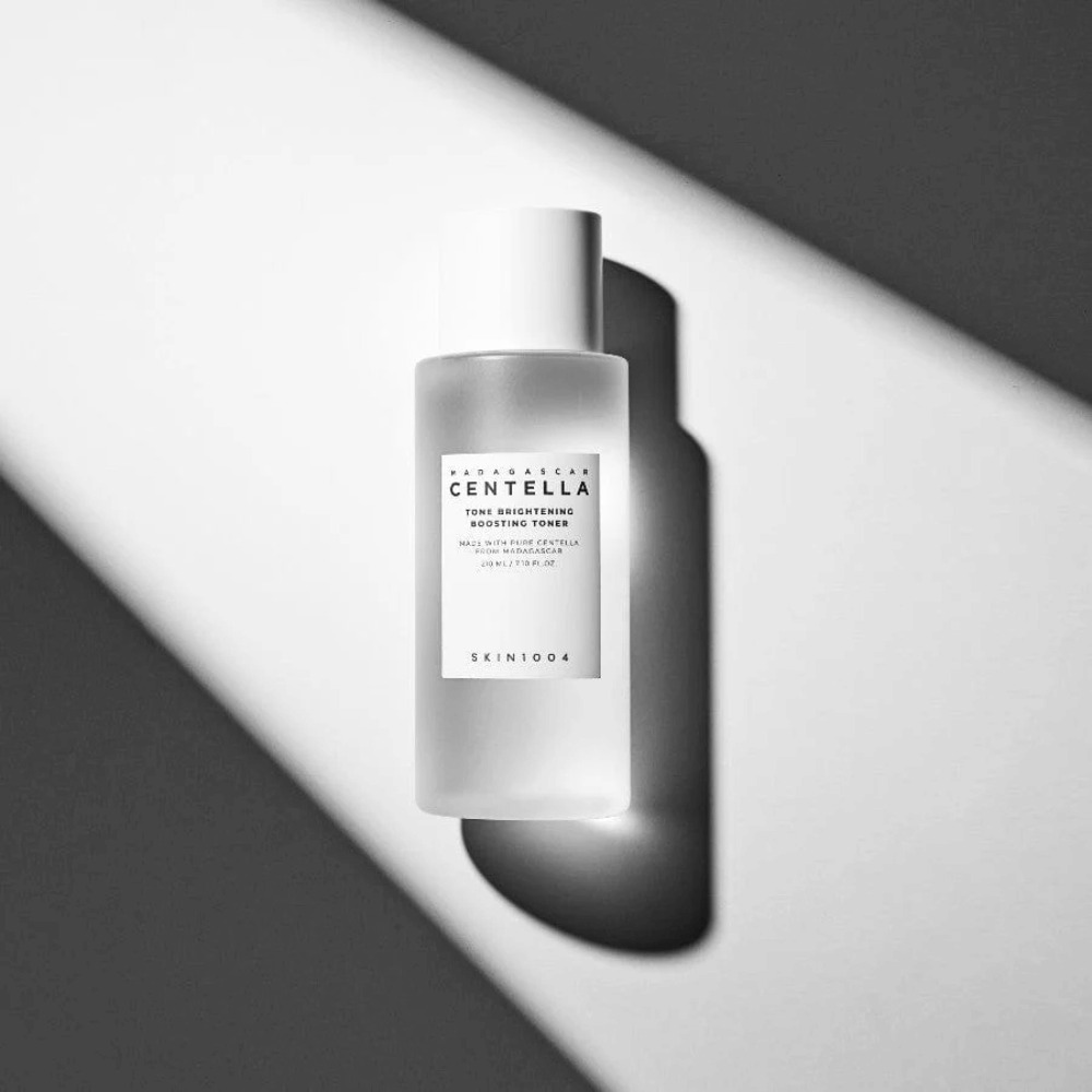 Flaske af SKIN1004 Madagascar Centella Tone Brightening Boosting Toner liggende på hvid overflade med dramatisk skygge i sort-hvidt lys.