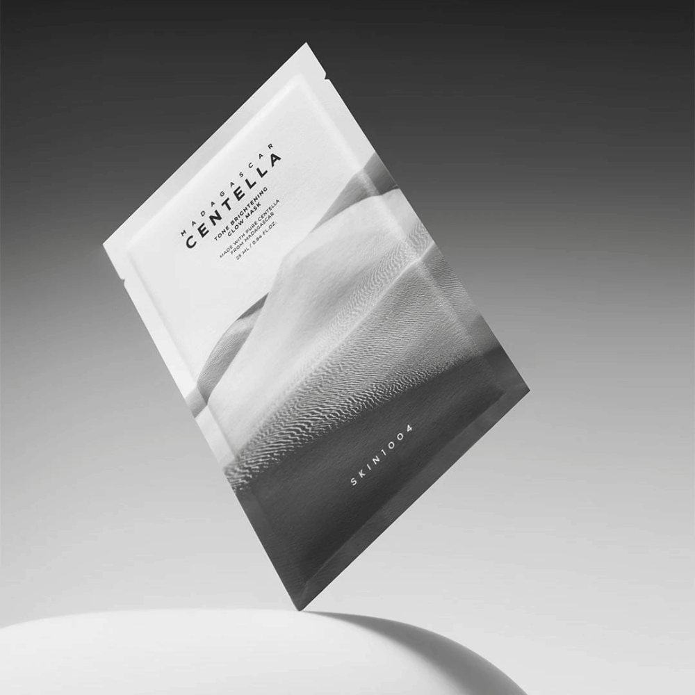 Sheet mask-emballage fra SKIN1004 svævende mod grå baggrund med minimalistisk design.