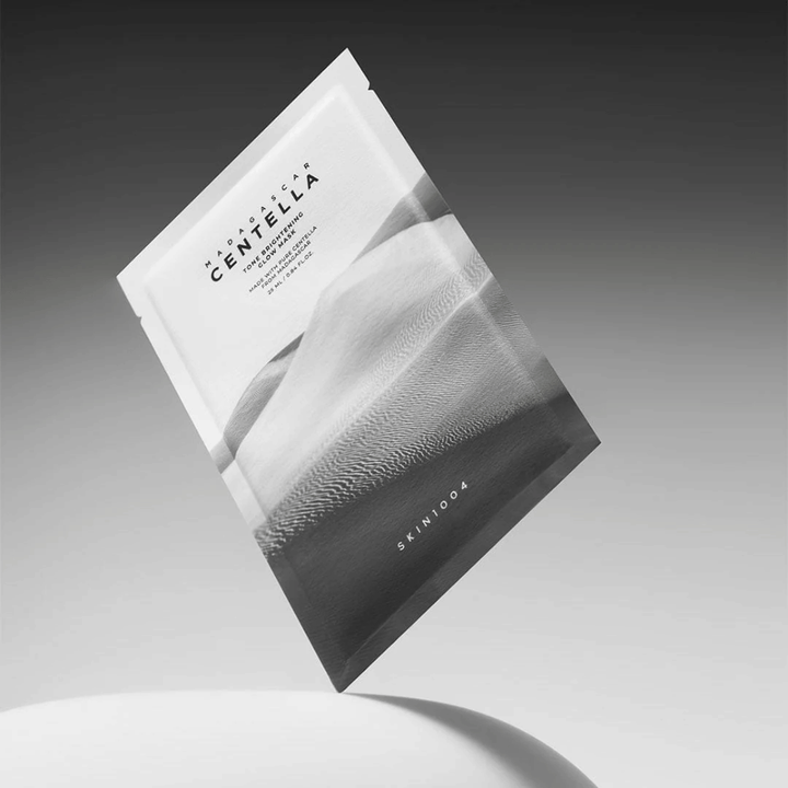 Sheet mask-emballage fra SKIN1004 svævende mod grå baggrund med minimalistisk design.