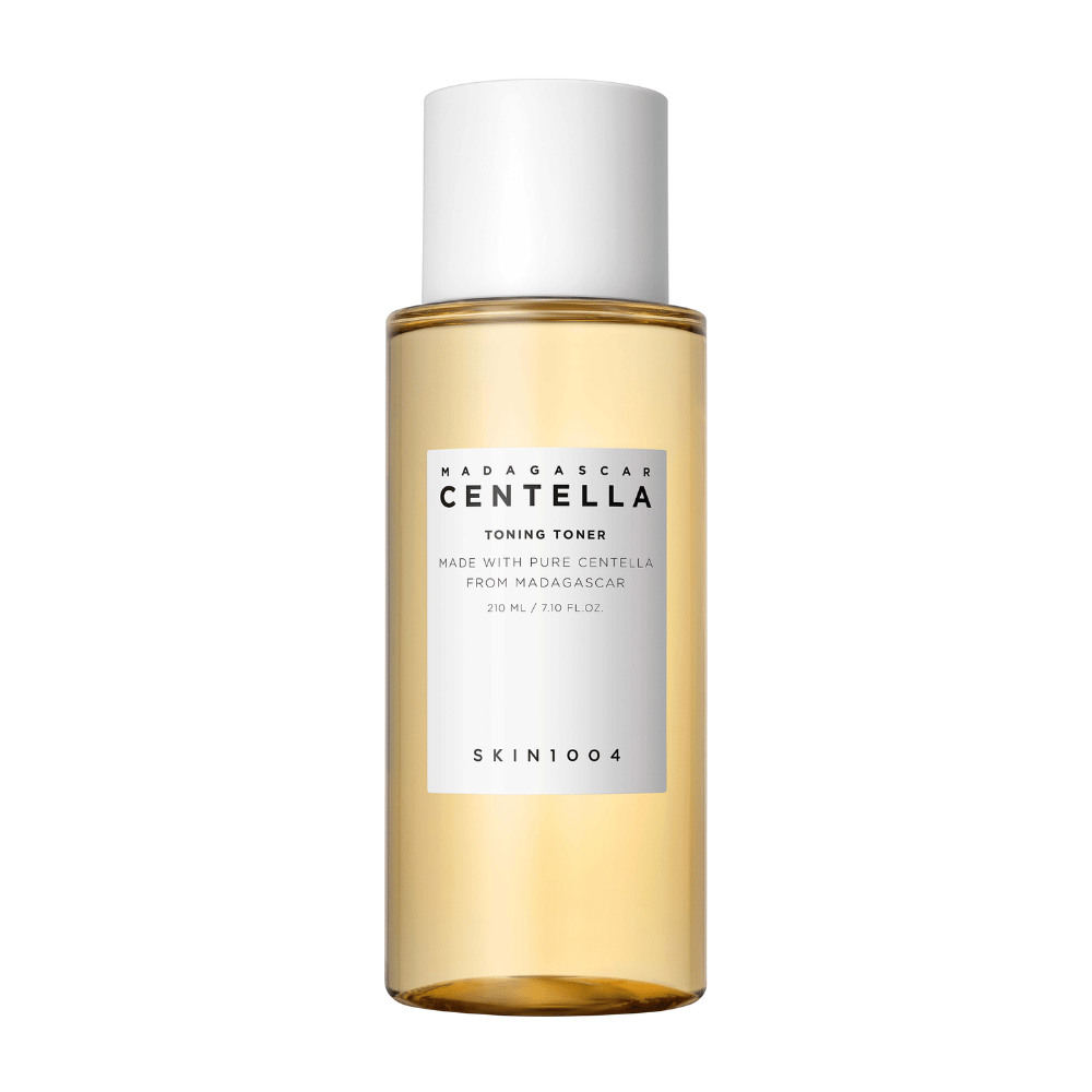 Billedet viser en flaske med hudplejetoner, mærket "Madagascar Centella Toning Toner" fra SKIN1004. Produktet er angivet til at indeholde 210 ml eller 7.10 fl.oz og er fremstillet med ren Centella fra Madagaskar. Emballagen er enkel og stilren med en gennemsigtig flaske og gylden toner væske indeni, hvilket giver en følelse af luksus og renhed. Varemærkets logo SKIN1004 er tydeligt synligt i den nederste del af etiketten.