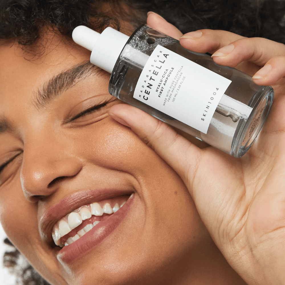 Smilende kvinde holder Skin1004 Madagascar Centella Hyalu-Cica First Ampoule ved siden af ansigtet.