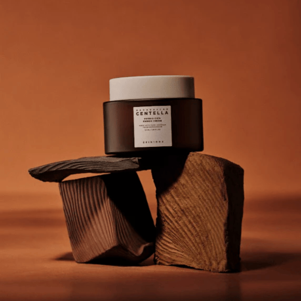 SKIN1004 Madagascar Centella Probio-Cica Enrich Cream i elegant brun glasbeholder på dekorative træblokke – nærende koreansk ansigtscreme, der styrker hudbarrieren.