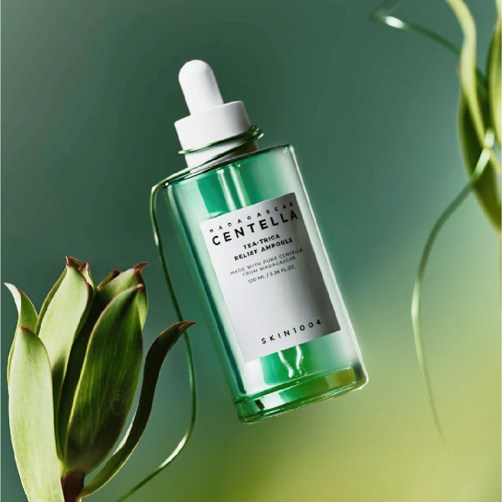 SKIN1004 Madagascar Centella Tea-Trica Relief Ampoule – grøn glasflaske med pipette, hvid etiket og 100 ml indhold, fotograferet mod grøn baggrund med plantemotiver.
