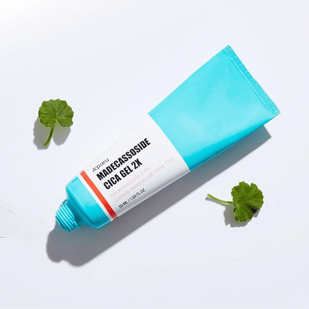 A’pieu Madecassoside Cica Gel 2X i blå tube med hvid etiket, omgivet af tre grønne centella asiatica-blade på hvid baggrund.