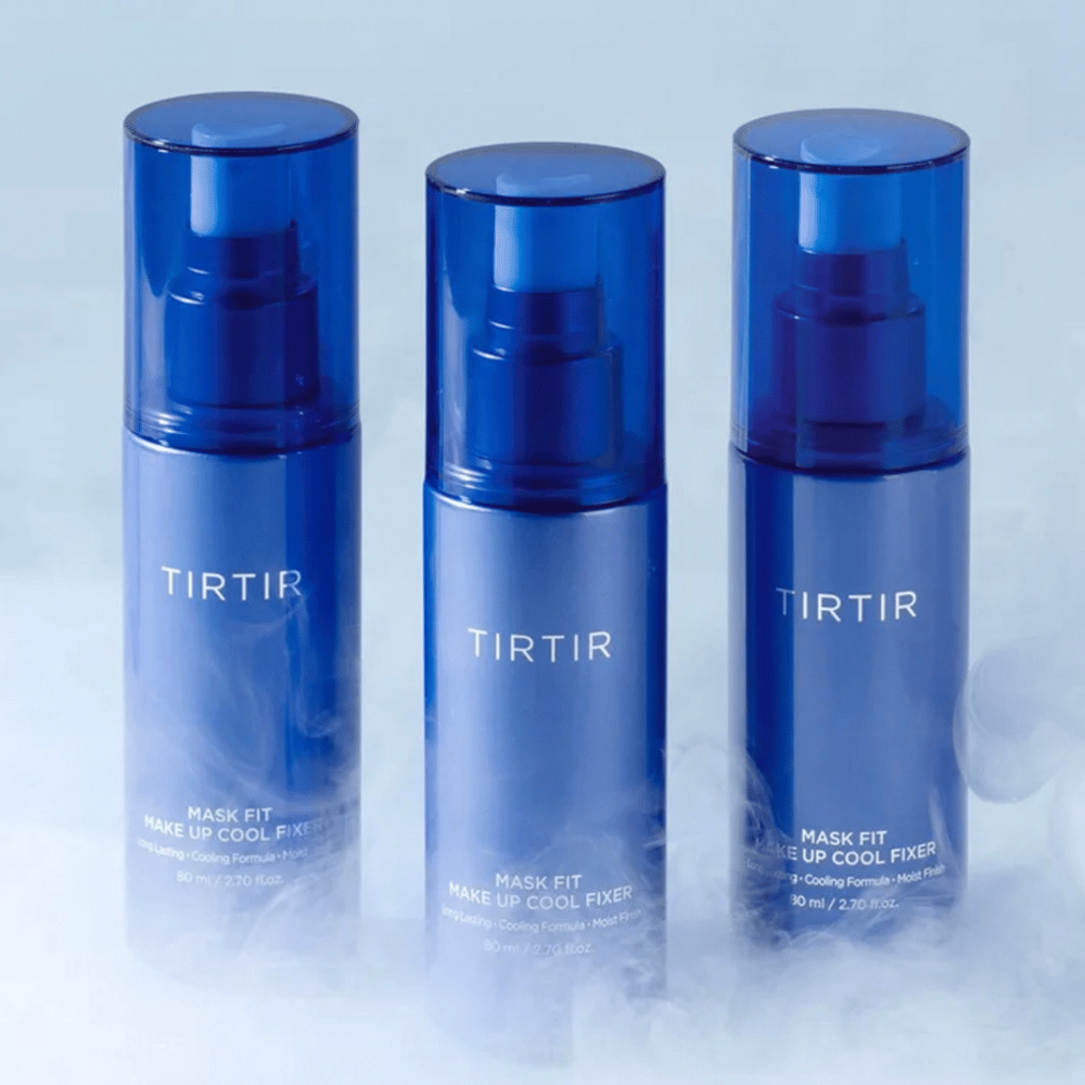 Tre blå sprayflasker med "TIRTIR Mask Fit Make Up Cool Fixer" på etiketten. Hver flaske rummer 80 ml (2,70 fl. oz.) og er designet til at give en kølende fornemmelse og langvarig makeup. Flaskerne står på en lys baggrund med tåge for at skabe en atmosfære af friskhed.