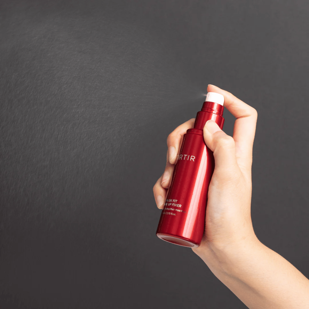 En hånd der holder en rød flaske af mærket tirtir Mask Fit Make Up Fixer og sprayer en fin tåge, ideel til at fixere makeup.