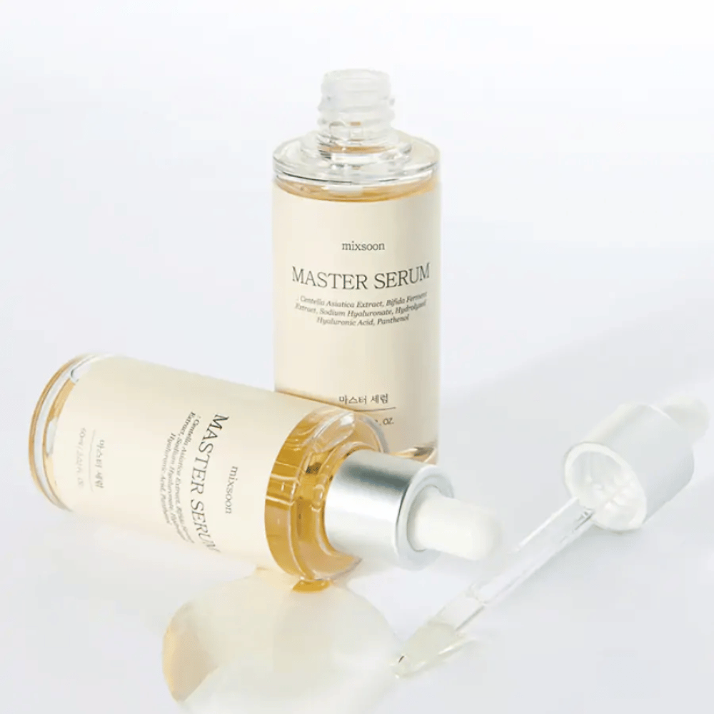 To flasker Mixsoon Master Serum, en stående og en liggende med åben pipette, hvor serumet er spildt ud på en hvid overflade.